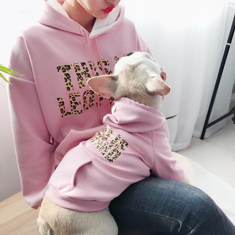Person wearing a pink hoodie with leopard print text, sitting with a small white cat also wearing a matching pink hoodie.