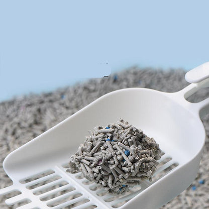 White scoop with gray cat litter on a blurred outdoor background