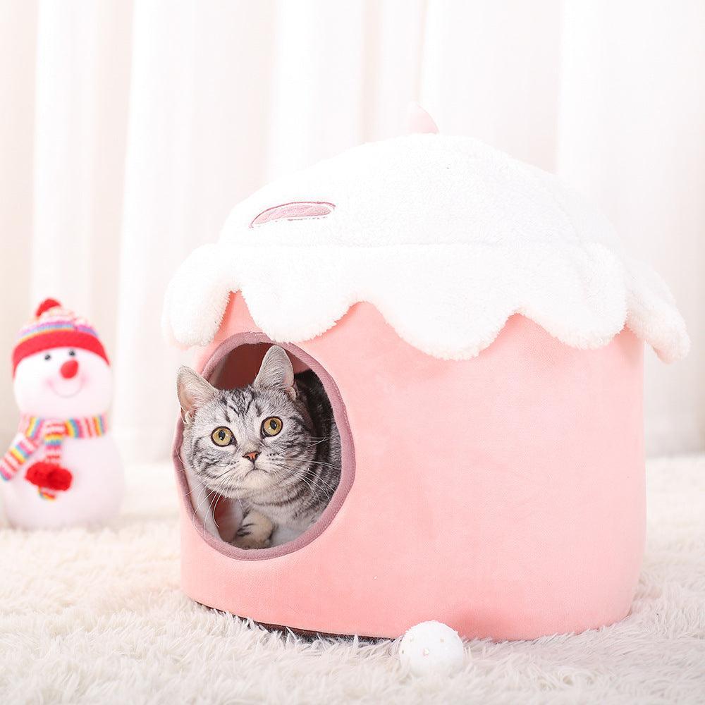 Cat peeking out from a pink pet house with a snowman toy in the background