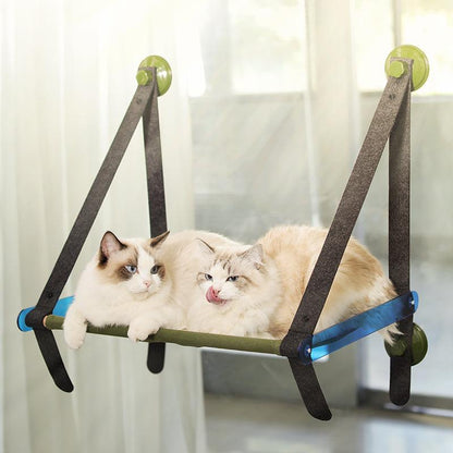 Two cats lounging on a triangular pet hammock with green balls on a white background