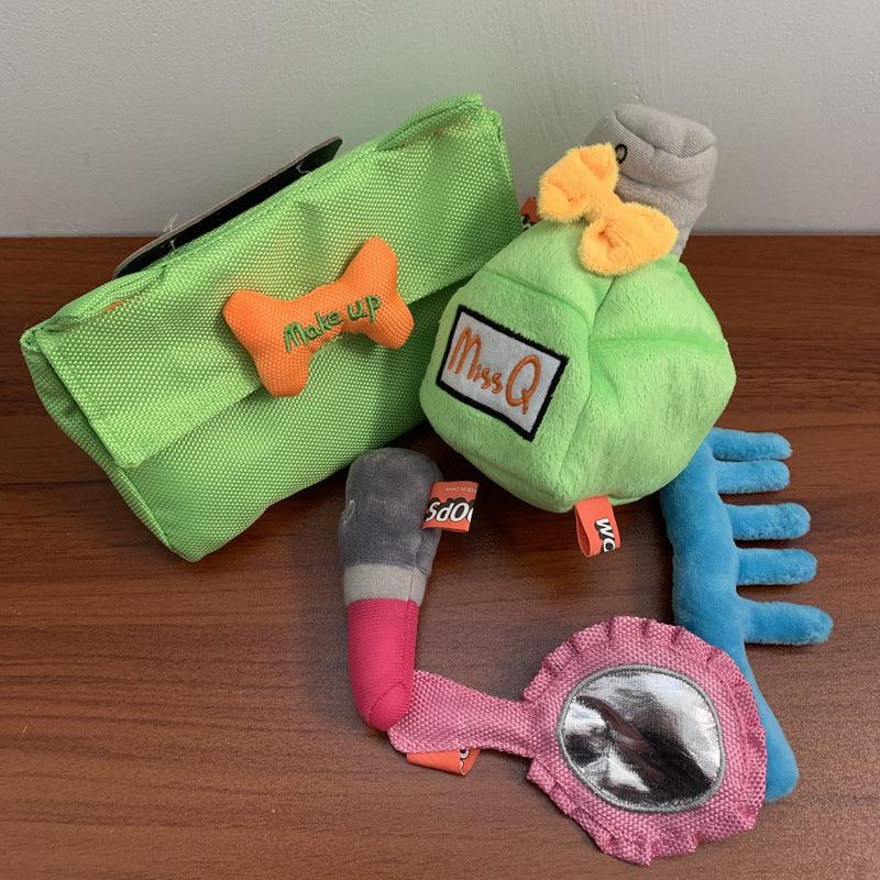 Colorful dog toys including a green plush toy, pink bone-shaped toy, and blue comb on a wooden surface.