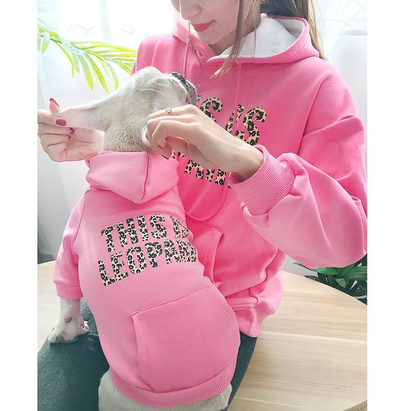 Person wearing a pink hoodie with leopard print text, holding a small dog in a matching hoodie.