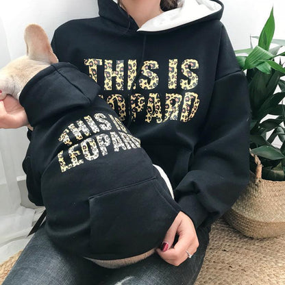 Person wearing a black hoodie with leopard print text, sitting on the floor with a dog.