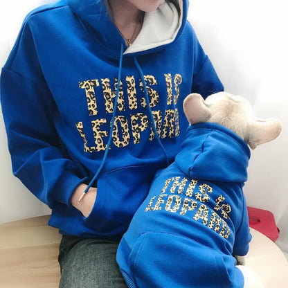 Person wearing a blue hoodie with leopard print text, sitting on a wooden floor.