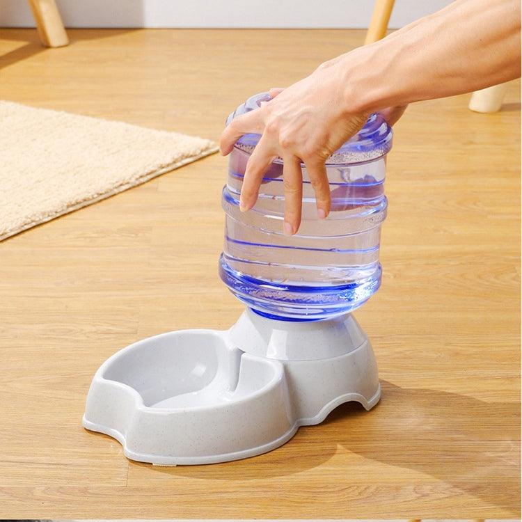 Pet water dispenser with a hand lifting the water bottle on a wooden floor.