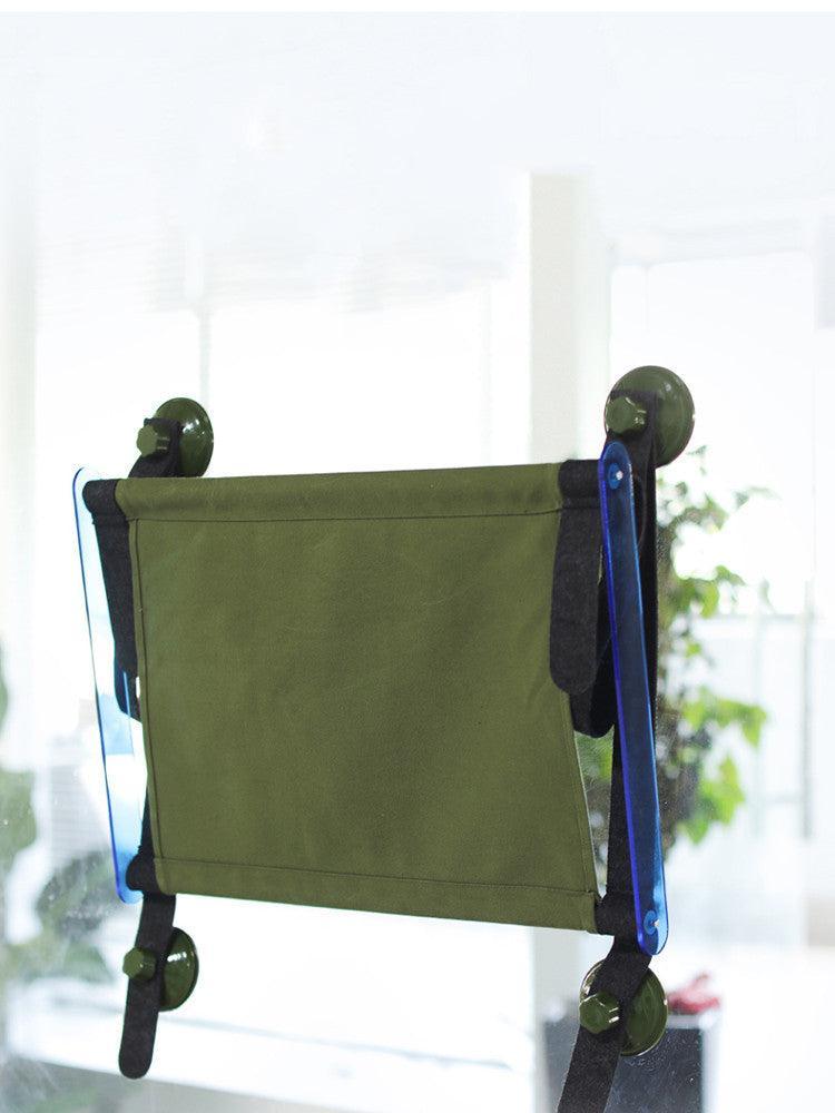 Green fabric bag with black straps and blue accents hanging on a white wall.